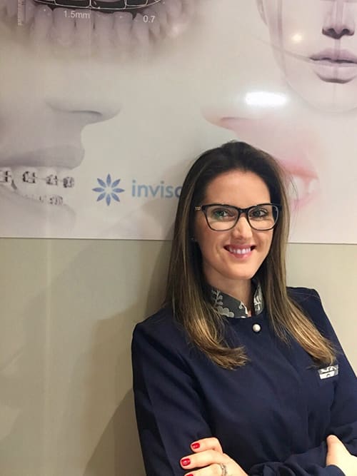 Dra. Clarice Pillon no consultório, diante de um painel Invisalign